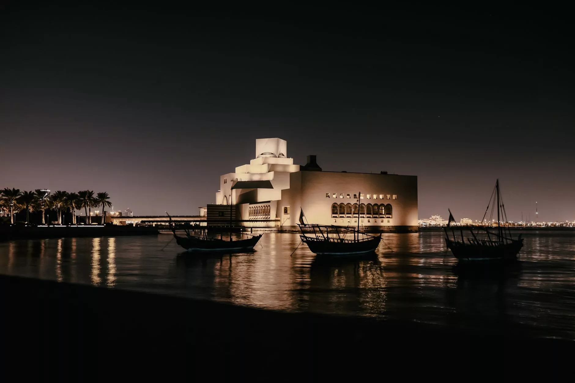Modern Doha silüeti ve geleneksel dhow teknelerinin körfezdeki gece görüntüsü