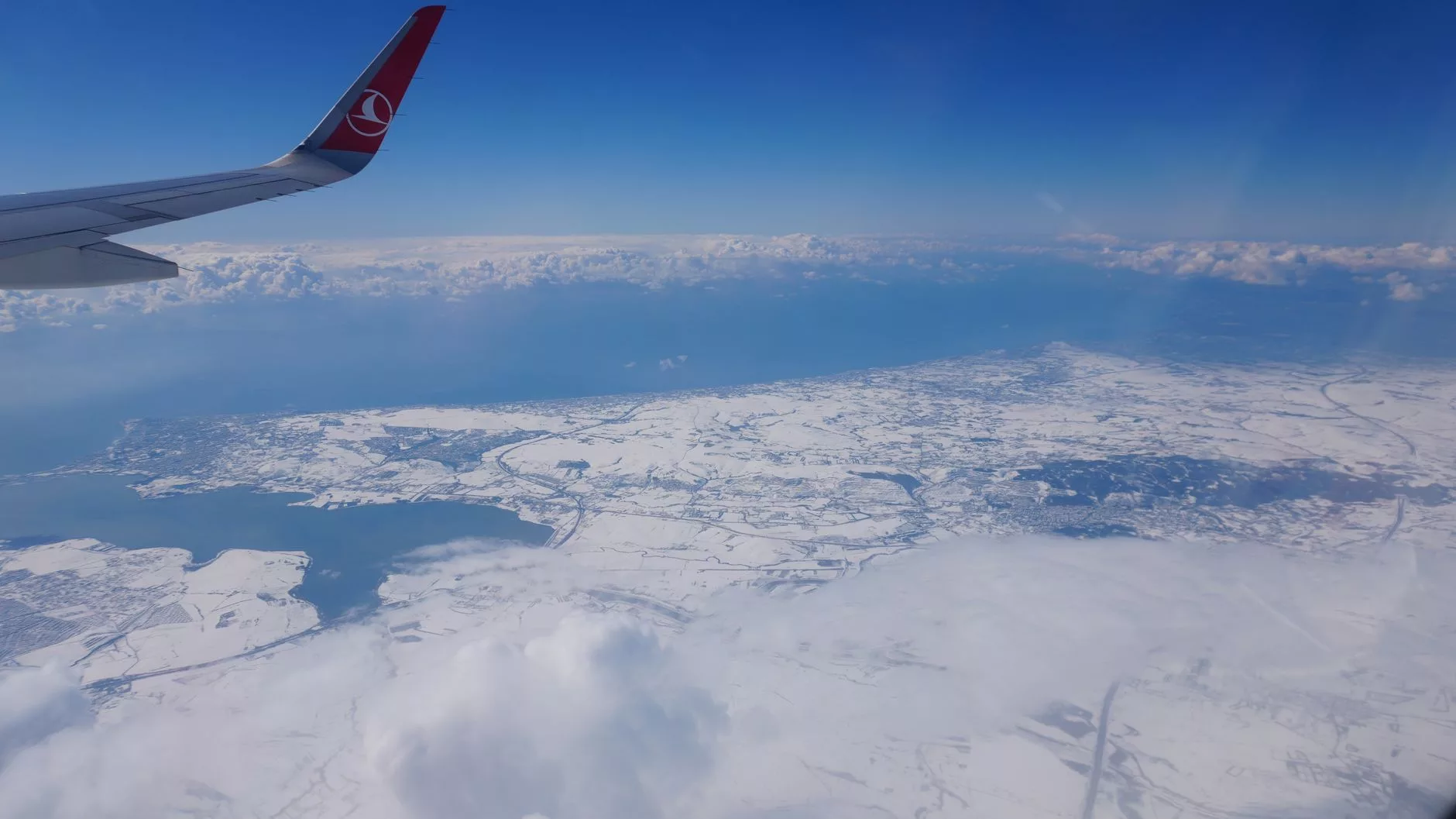 Bulutların üzerinden Girit sahillerine yaklaşan bir uçak kanadı görüntüsü
