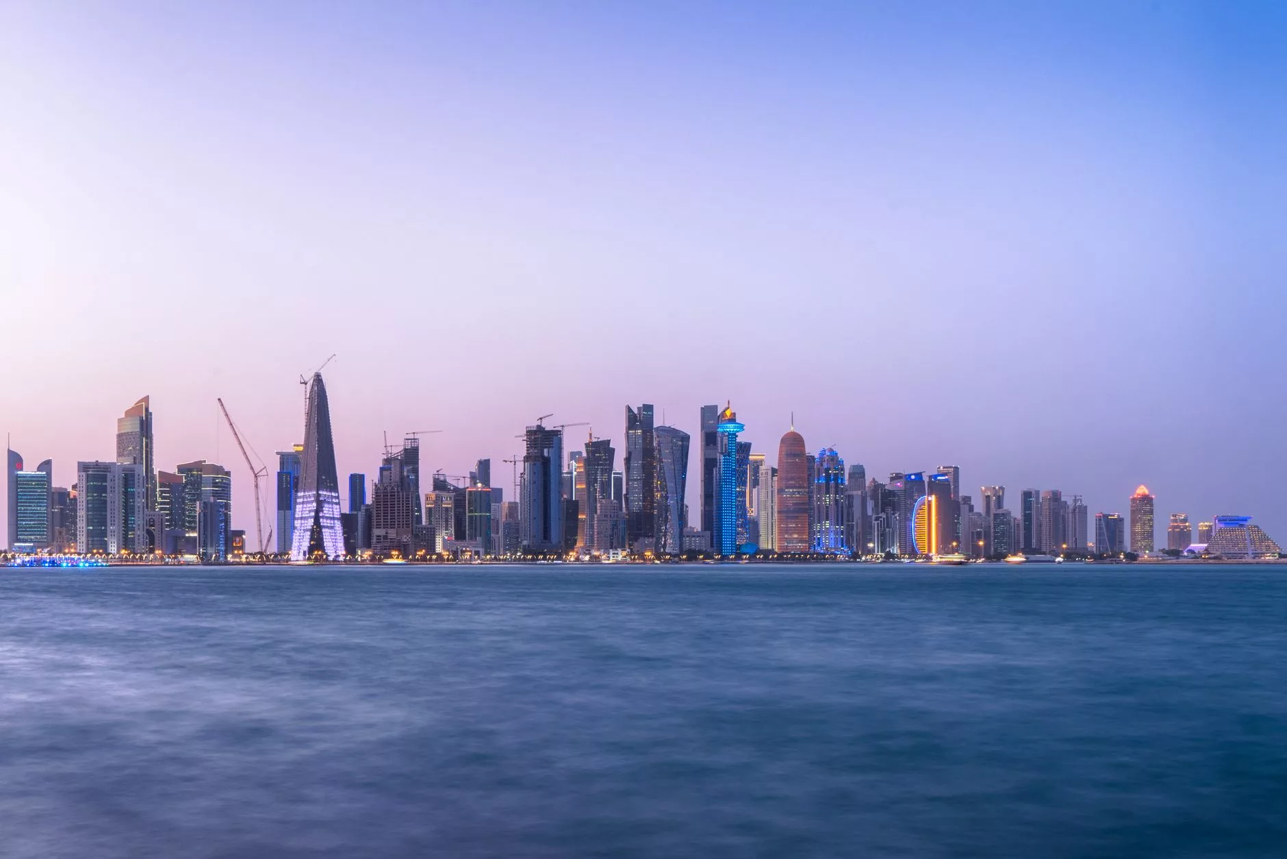 Doha Corniche sahil şeridinde gün batımı ve modern silüet