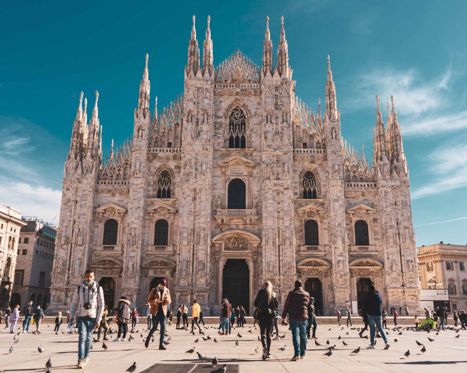 Milano sokaklarında sonbahar yaprakları altında yürüyen bir gezgin ve arkada Gotik katedral silueti