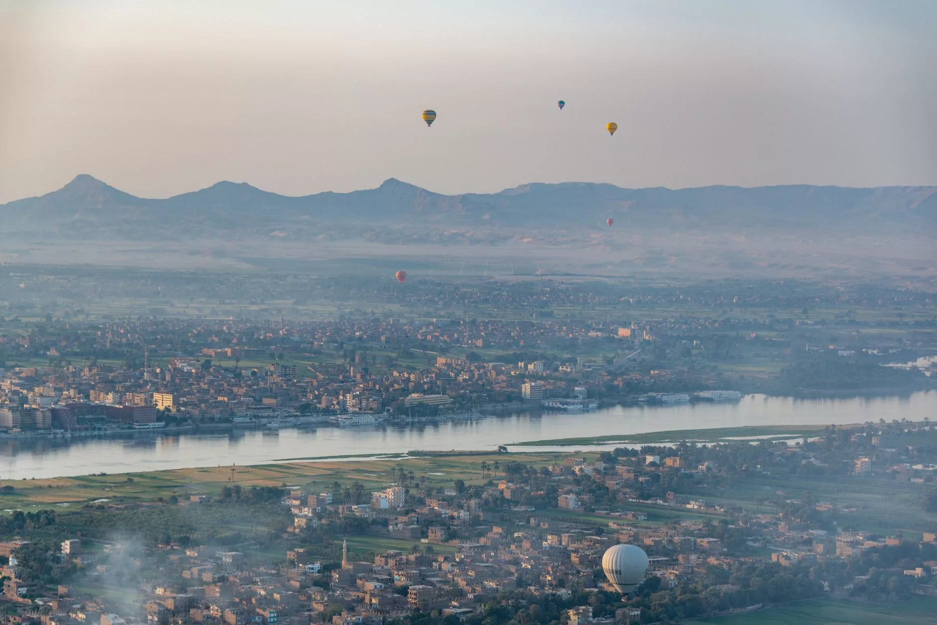 Kahire üzerinde süzülen sıcak hava balonları ve uzaktaki Giza piramitleri sabah sisinde
