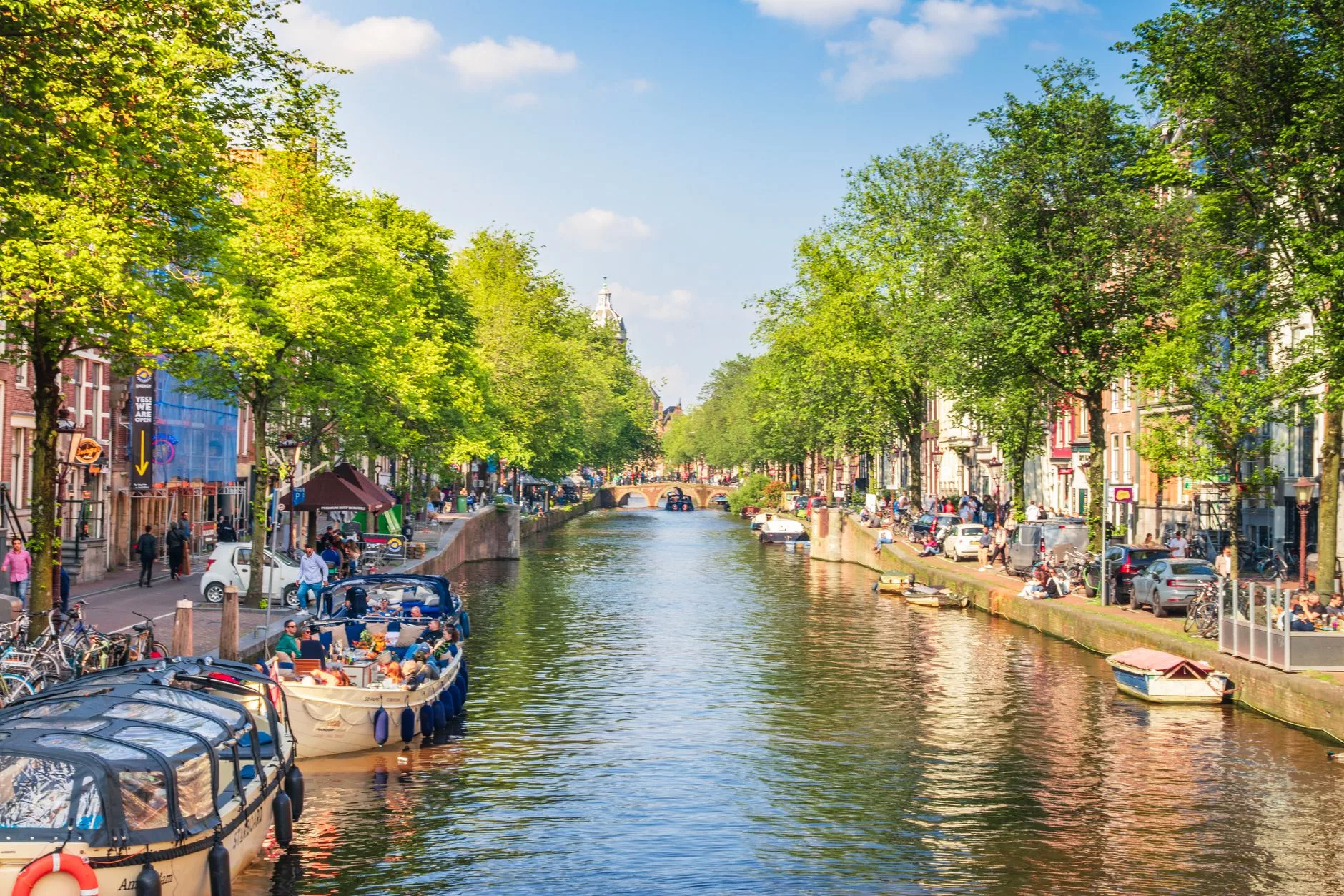 Amsterdam kanal kenarında oturan ve patates kızartması yiyen turistler