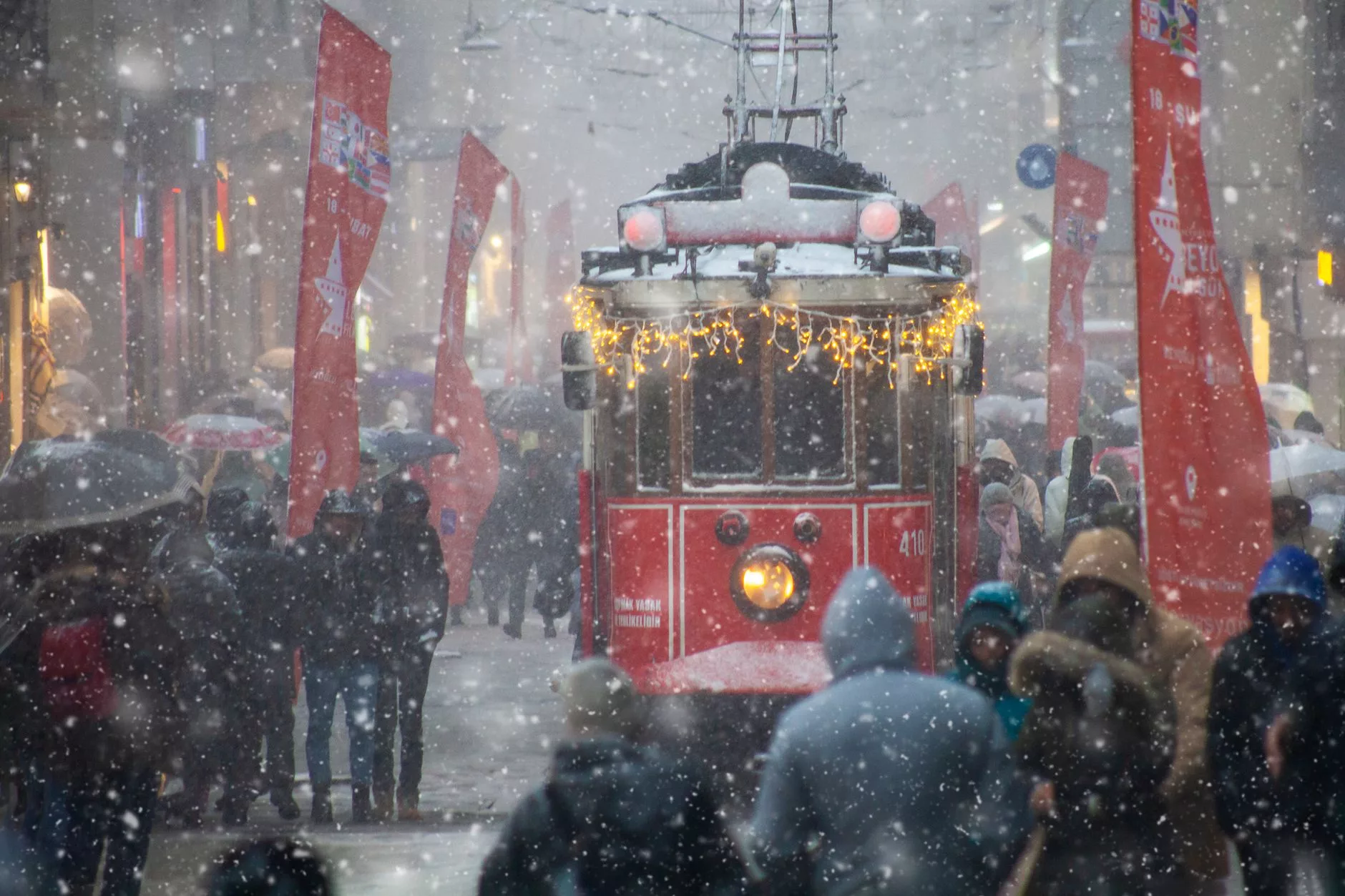 Karlı bir Avrupa şehrinde ilerleyen kırmızı bir tramvay